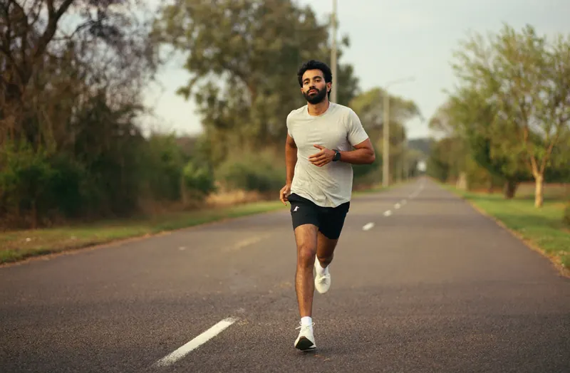 A man runs down an empty tree-lined road in warm golden-hour light